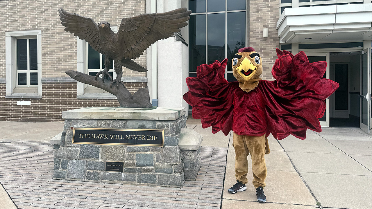 The new Saint Joseph’s Hawk, flapping his wings next to a statue of a real Hawk, with the slogan THE HAWK WILL NEVER DIE