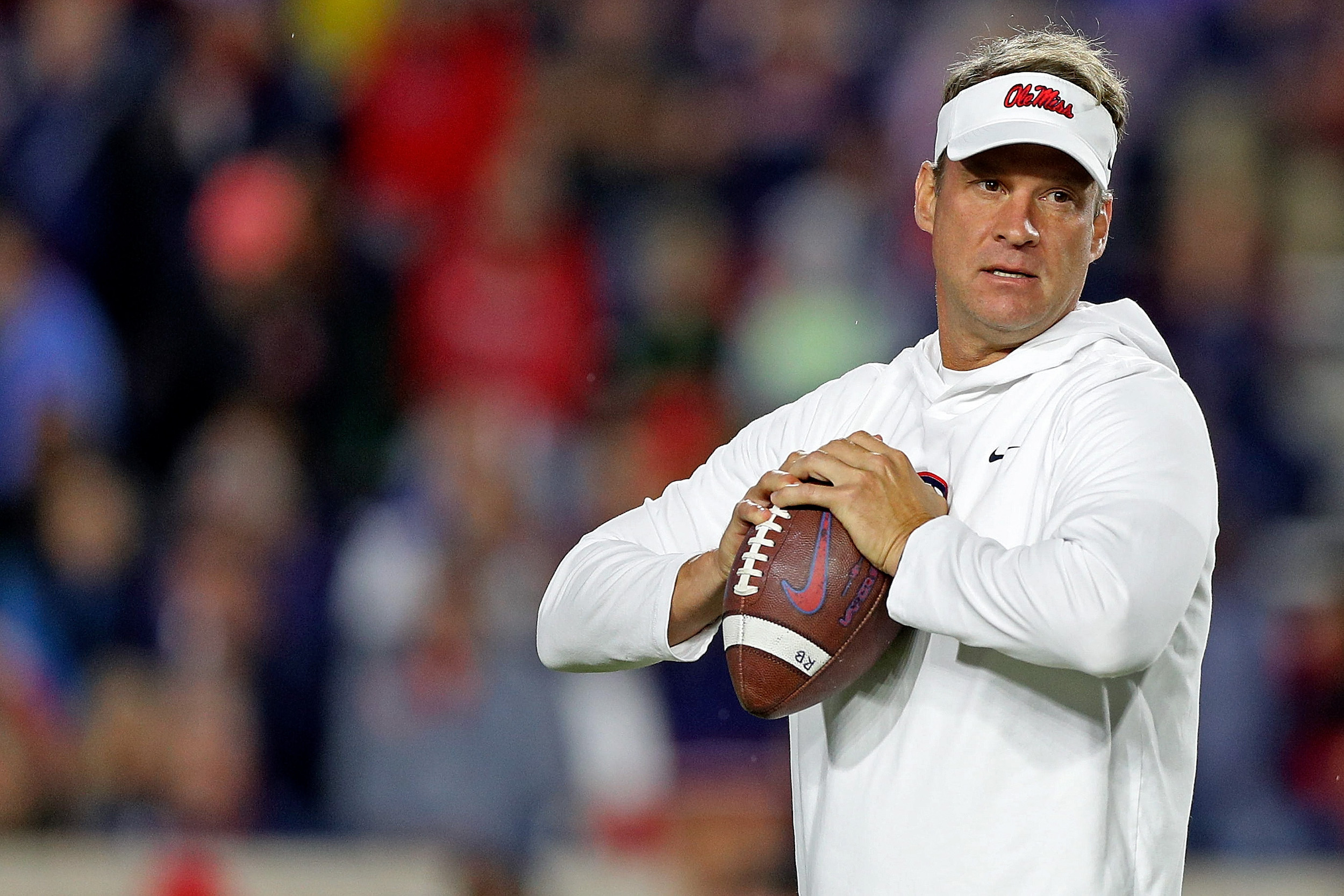 Lane Kiffin wears a visor and holds a football.
