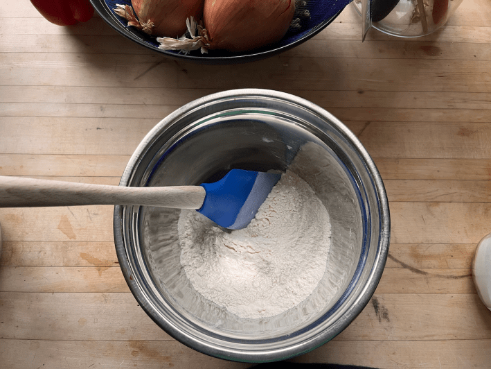 A bowl with the dry ingredients for hogugwaja batter with a rubber spatula resting on the side.