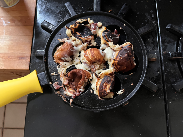 A mess of hogugwaja batter in various states of cookness (from raw to burnt) exploding over a cast iron ebelskiver pan.