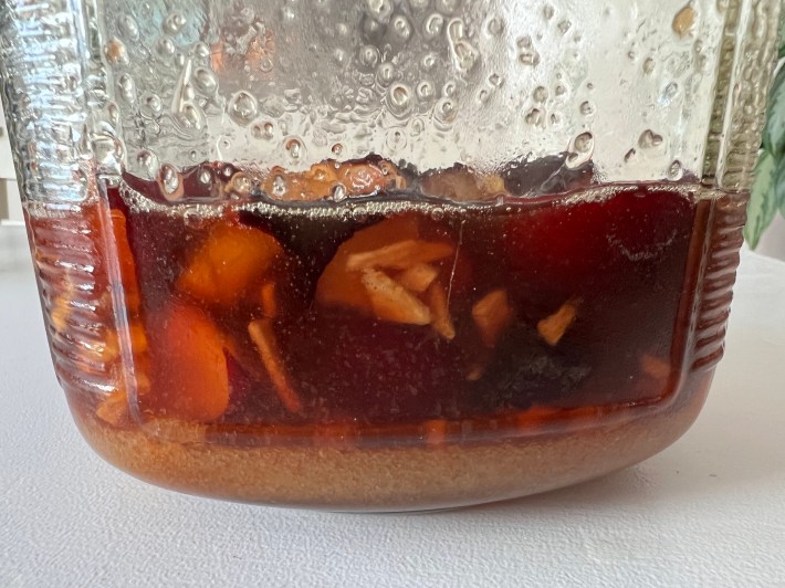 A side view of the syrup, showing fruit floating near the surface and a half-inch or so of undissolved sugar along the bottom.