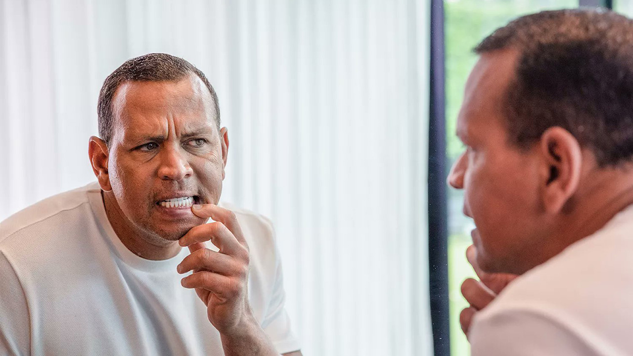 Alex Rodriguez looks at his teeth, with this hand pulling one of his lips back, and you see him in the mirror and also see the back of his head.