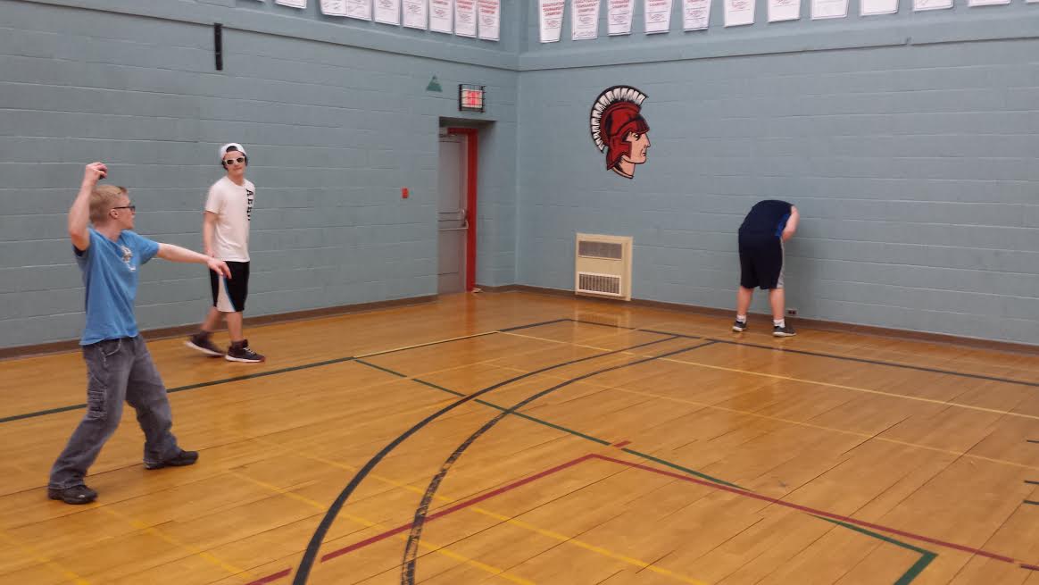 Three teens playing butts up, with one hunched over at the wall preparing to have a racquetball get thrown at his butt, per the rules.