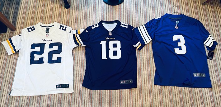 Three Vikings jerseys: On the left, a white one from the old NFL shop. In the middle, a purple one from Fanatics. On the right, a purple one from DHGate.