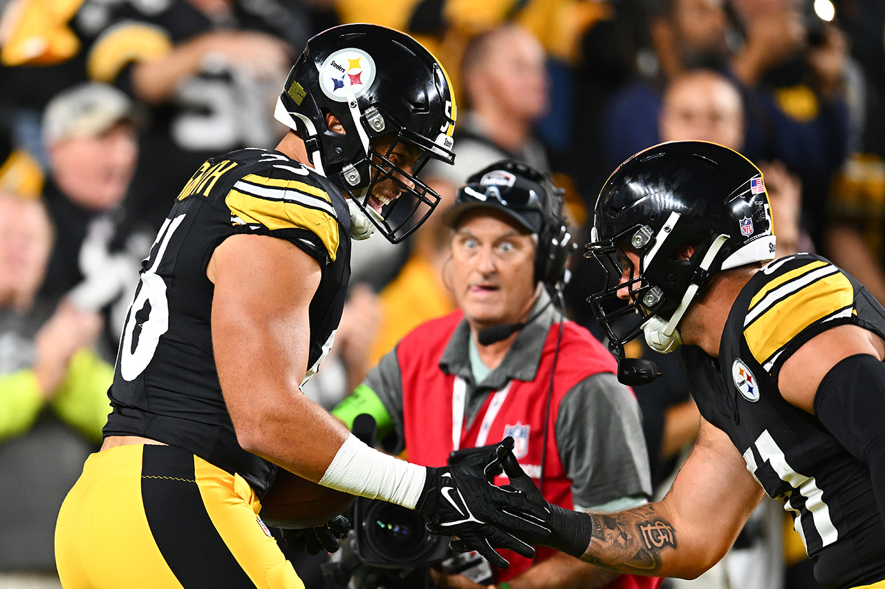 Alex Highsmith #56 of the Pittsburgh Steelers is congratulated by Nick Herbig #51 after scoring a touchdown after an interception against the Cleveland Browns during the first quarter at Acrisure Stadium on September 18, 2023 in Pittsburgh, Pennsylvania. Steelers in black jerseys with yellow trim, black helmets. Fans behind them. Also behind them: There is a cameraman in the center who has his tongue out and is making kind of a funny face. Ok, a very funny face.