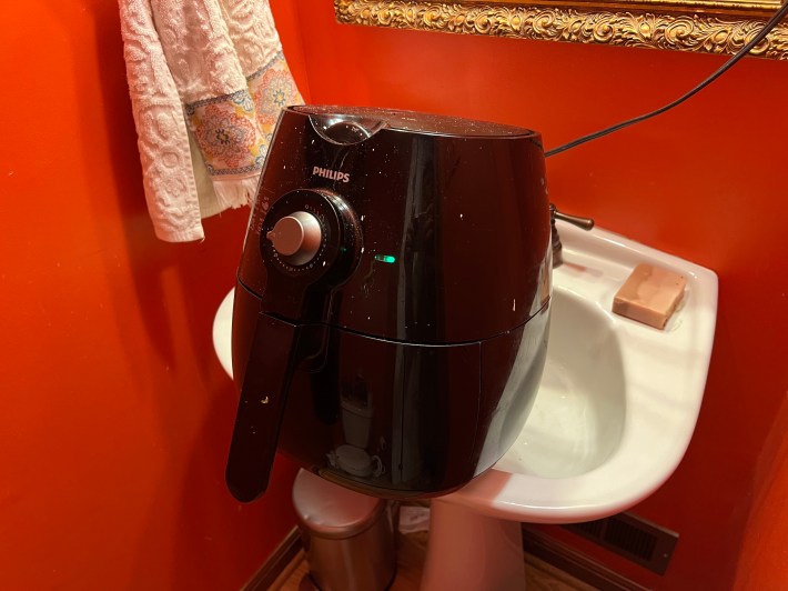 An activated air-fryer rests unevenly in a small bathroom sink.