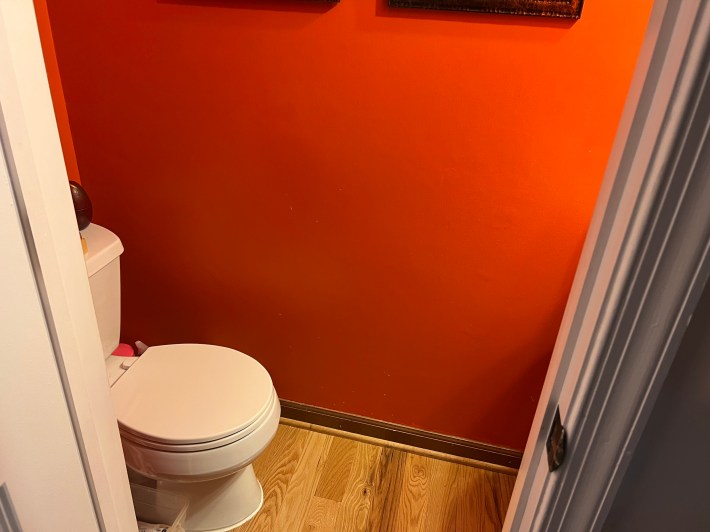A small bathroom with a red wall and a toilet.
