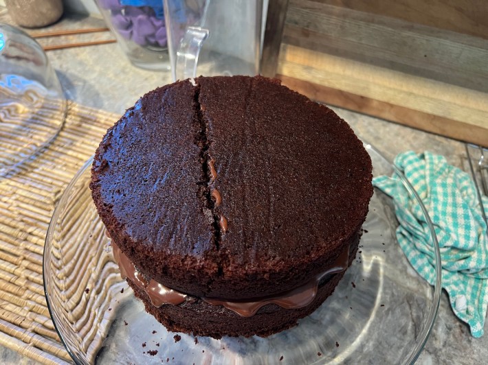 A top sponge broken cleanly into two pieces rests atop a wet layer of ganache, which rests atop a bottom sponge.