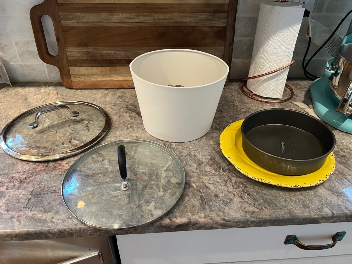 Atop Chris's countertop are five options for circle shapes: A plastic plate, a cake pan, two pot lids, and a lamp shade.