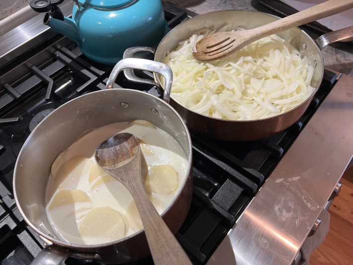 Onions cook in a sauté pan next to sliced potatoes simmering in milk and cream in a saucepan.