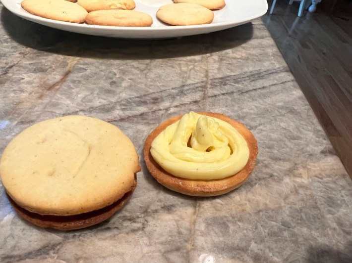 Yellow custard squeezed in a swirl pattern onto the interior side of a cookie, sitting next to a filled, completed sandwich cookie.