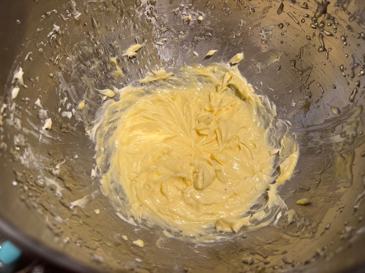 A buttery yellow custard with dots of vanilla sits at the bottom of a messy metal mixing bowl.