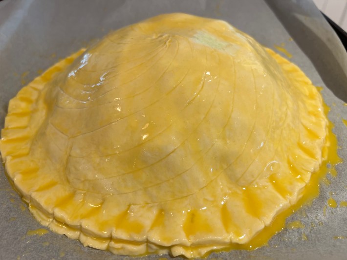 An assembled pithivier, mounded with filling and glazed with egg, before baking.