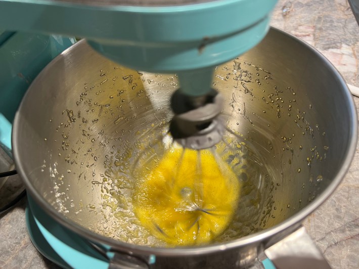 A stand mixer furiously whisks egg yolks and hot sugar syrup.