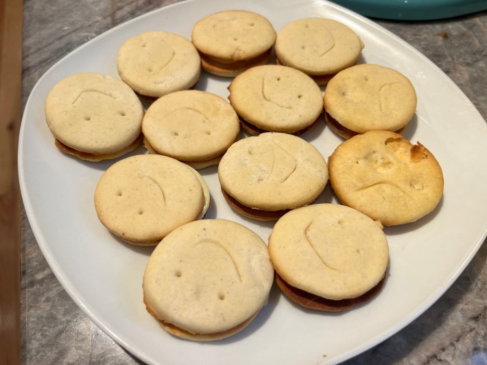 12 completed Custard Cream sandwich cookies, showing smiles and frowns, including one that is badly mangled.