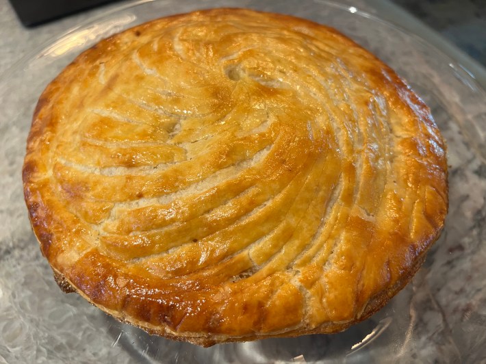 A finished pithivier, on a cake stand, on a countertop.