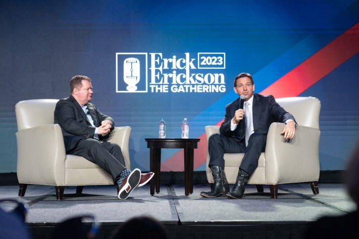 DeSantis wears humongous black boots while seated on stage. The toes appear virtually flat and far too long for his feet.