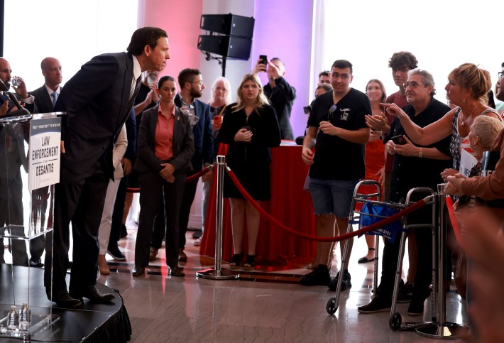 DeSantis leans forward on stage to take a question during an event. The toe of his left shoe is dramatically curled, and his right shoe appears to be loosely hanging onto his foot in such a way that it is hard to imagine how his foot could be all the way in there.