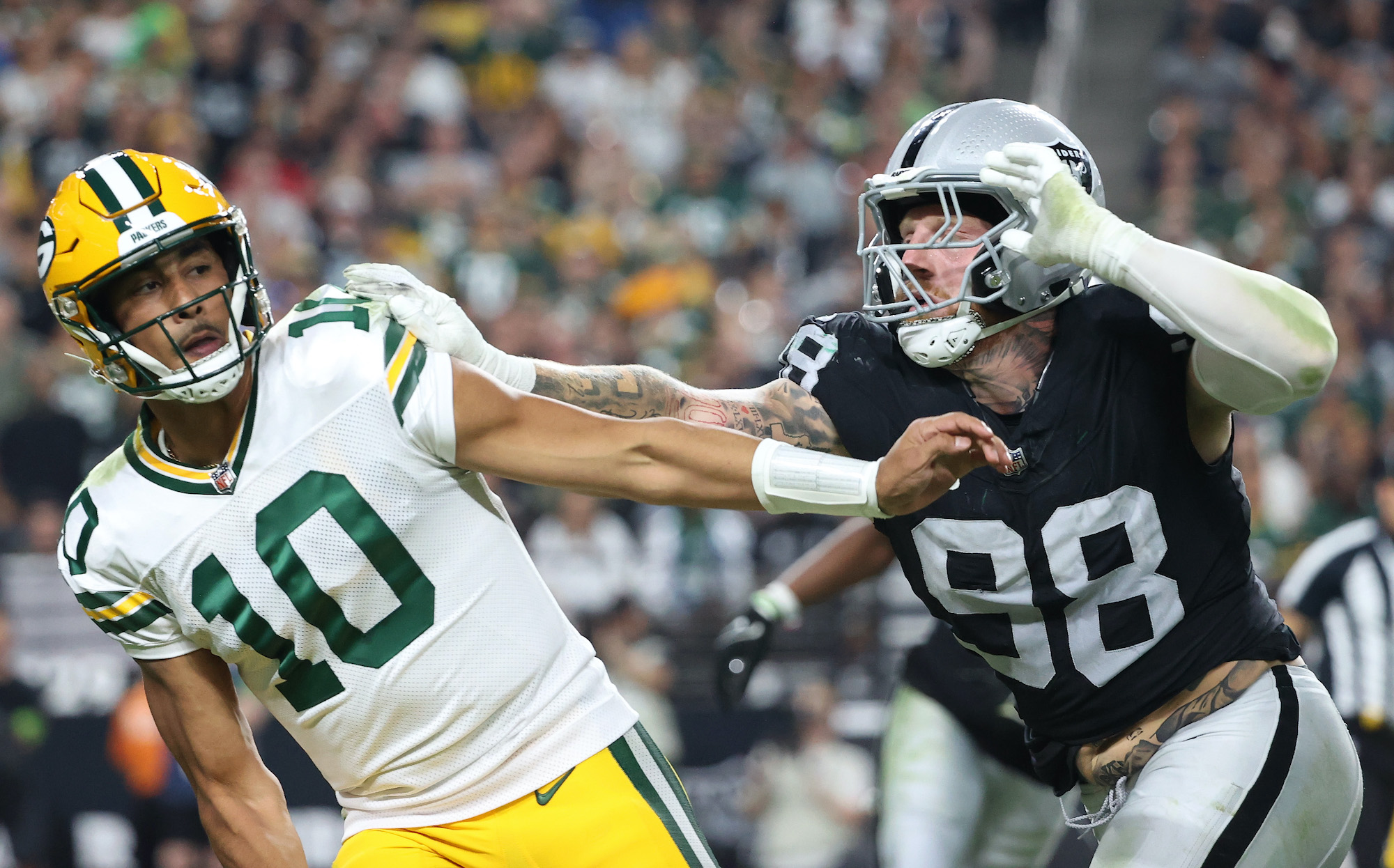 Jordan Love is pushed by a Raiders defender after throwing a pass.