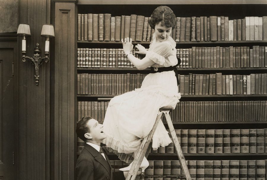 a woman in a dress sits on a library ladder