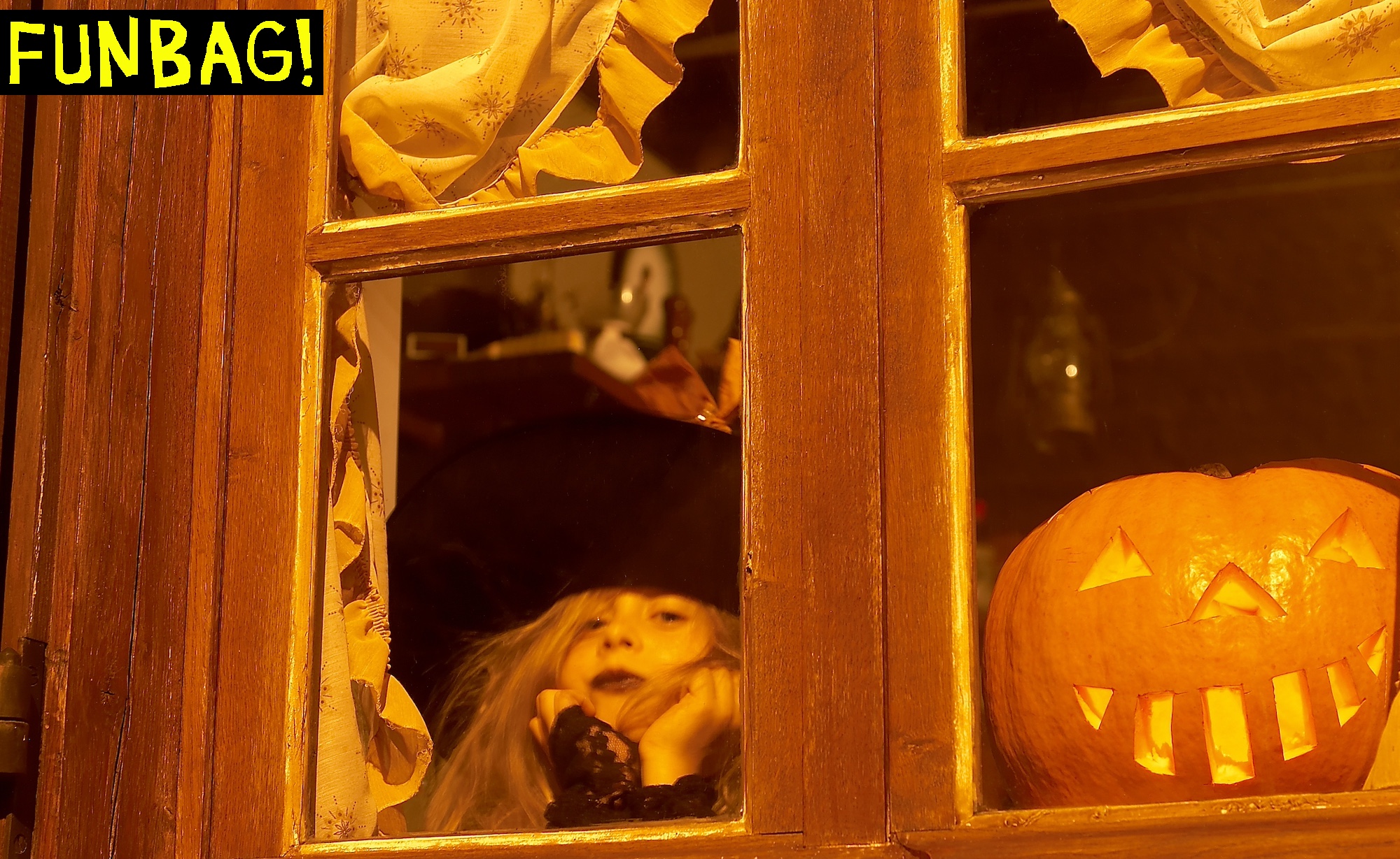 A little girl in a witch outfit and a jack-o-lantern are in a spooky window