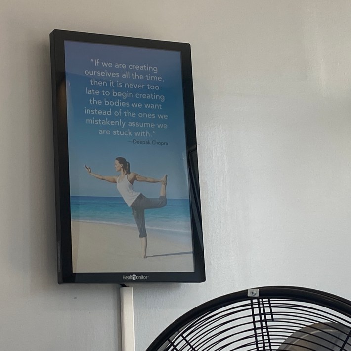 A tablet on the wall showing a person doing yoga along with a quote from Deepak Chopra: “If we are creating ourselves all the time, then it is never too late to begin creating the bodies we want instead of the ones we mistakenly assume we are stuck with.”