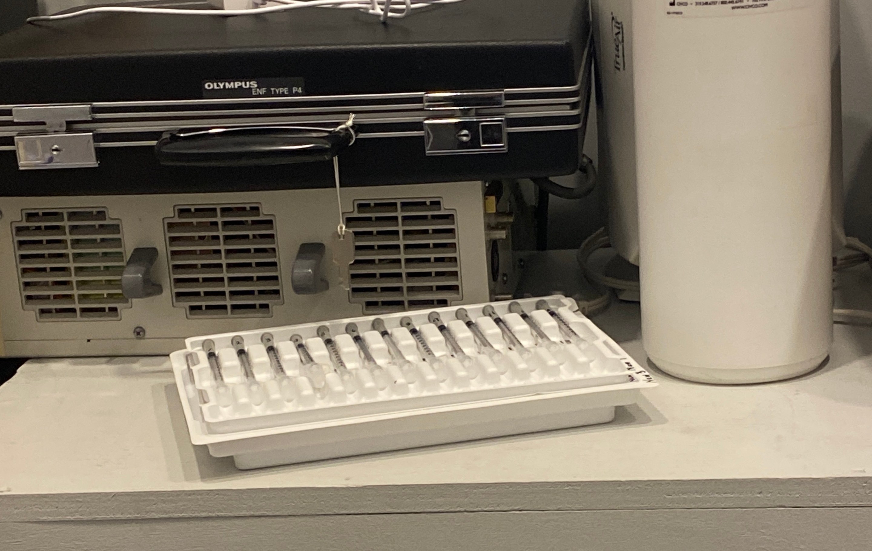 A photo of a white tray full of 13 little syringes, which is sitting on top of an unseen white tray of even more syringes