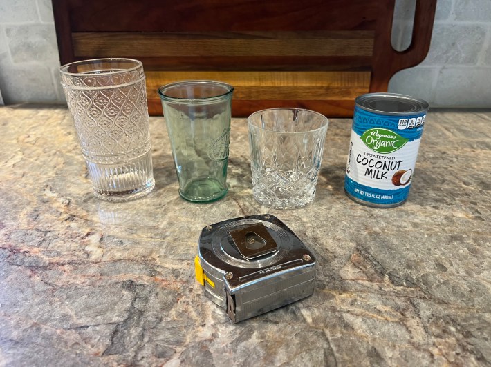 Three clear glasses of different sizes, one unopened can of coconut milk, and a tape measurer sit on Chris's countertop.