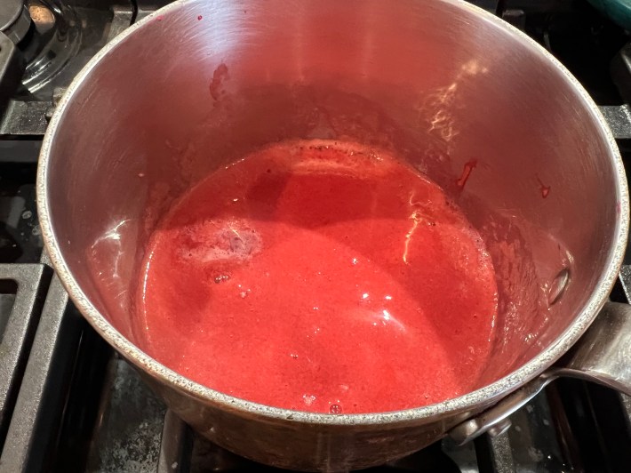 Pink foamy raspberry purée simmers in a small saucepan.