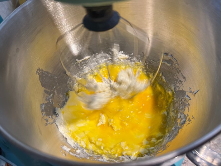 A stand mixer mixes eggs and cream cheese with sugar.