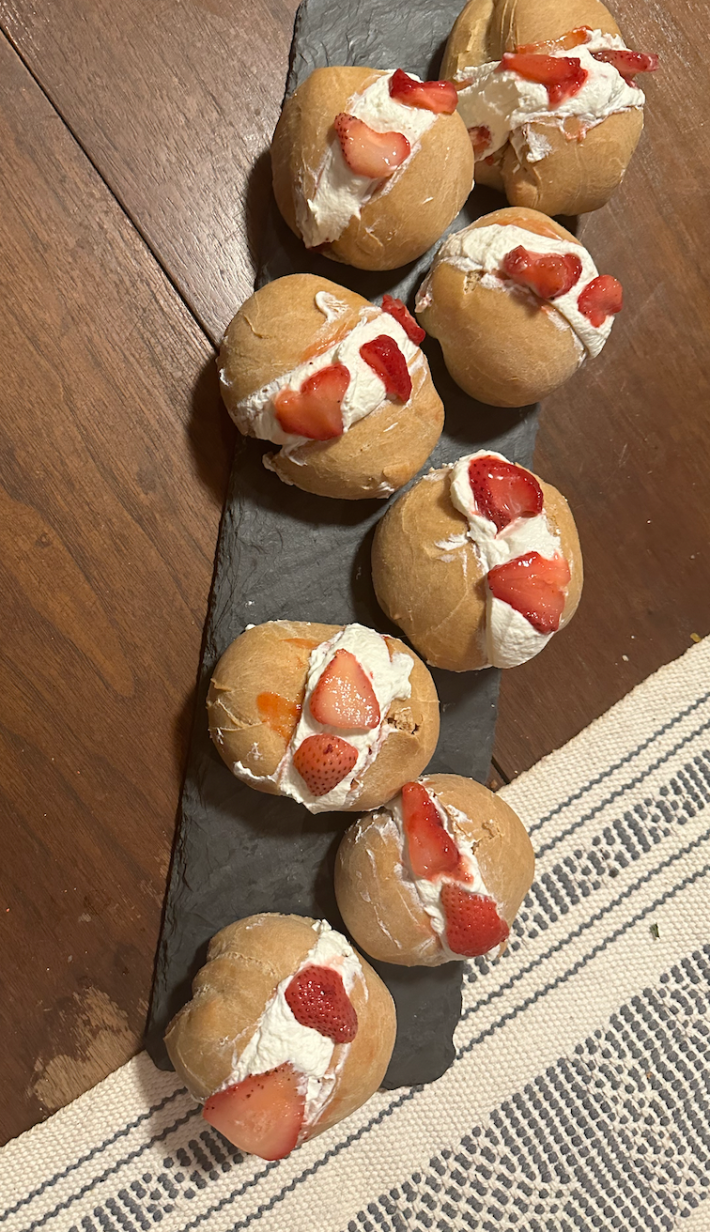 eight buns filled with cool whip and topped with strawberries on a slate tray