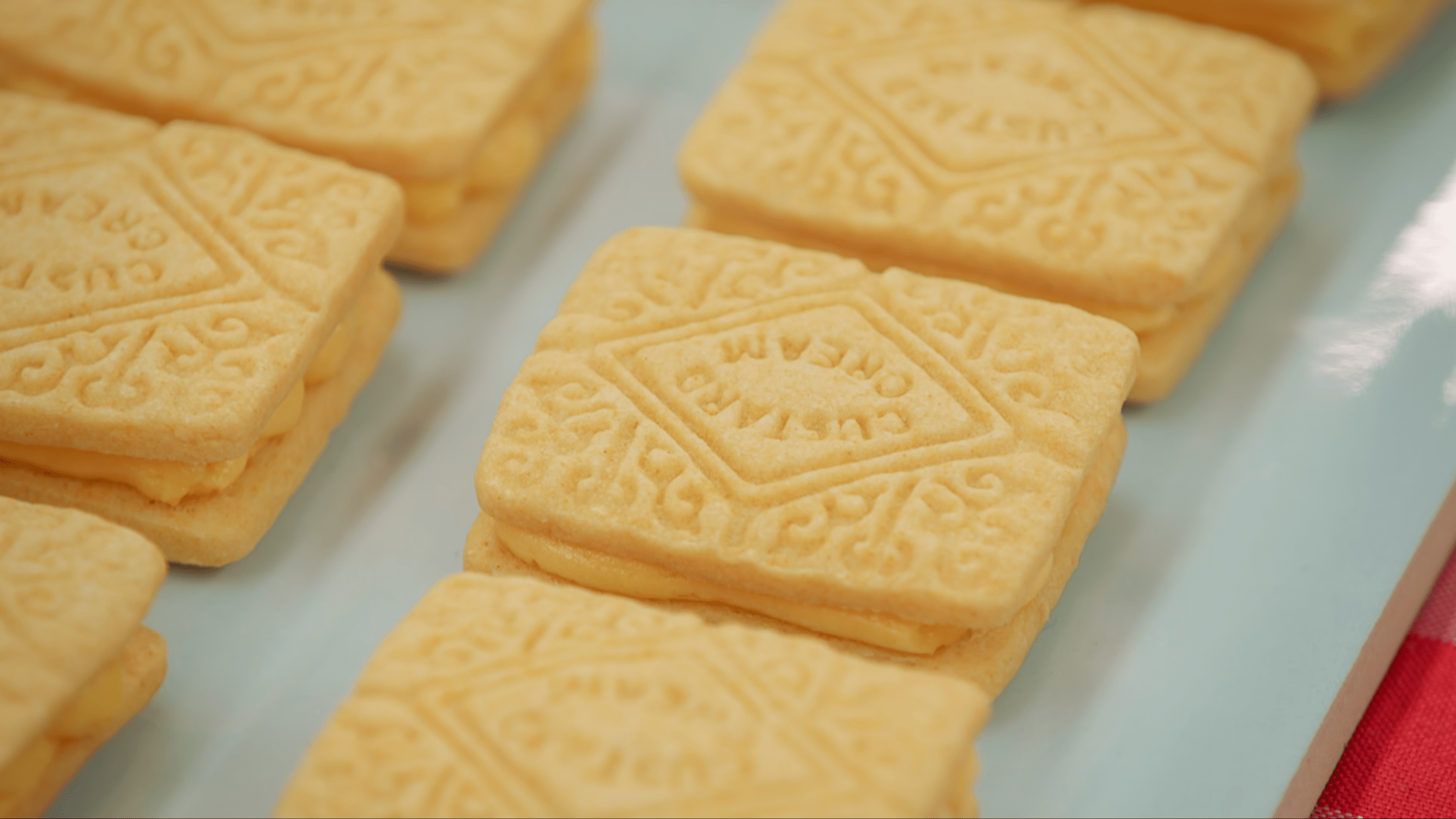 A well-made Custard Cream cookie from the show, with a clean stamped pattern that says "CUSTARD CREAM."