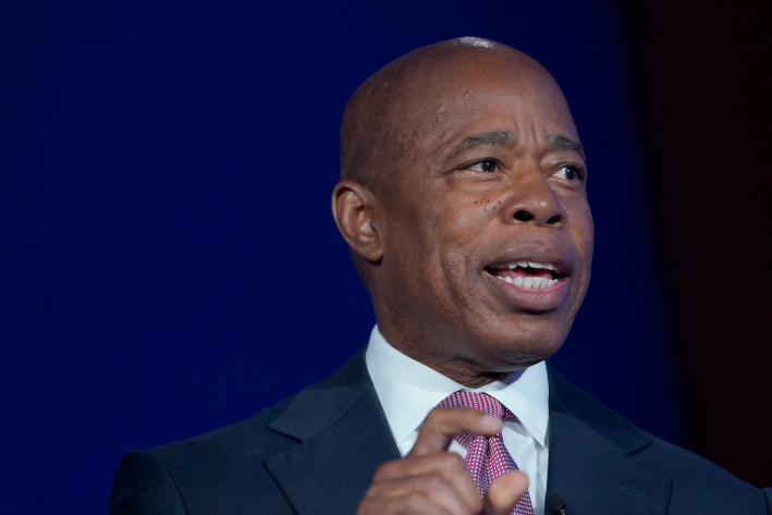 NYC mayor Eric Adams making a pinching gesture with his right hand, while addressing a crowd at some type of summit.