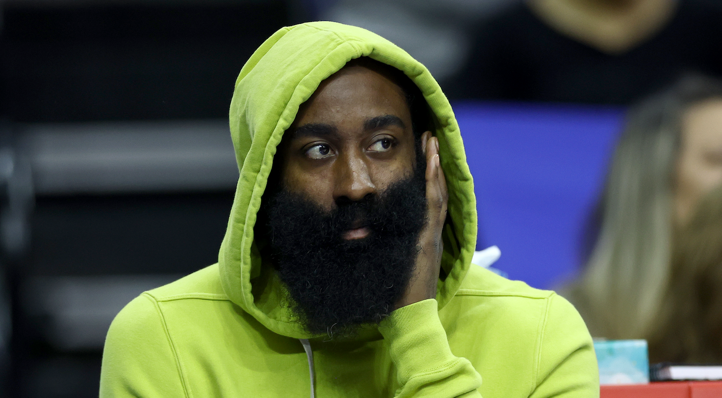James Harden, in a dayglo green hoodie, watches a game from the bench.