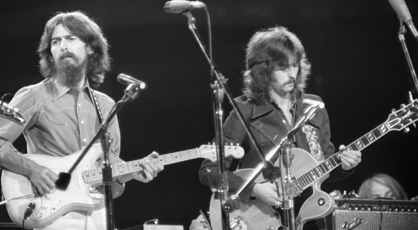 George Harrison and Eric Clapton, playing their guitars, in a black-and-white concert photo from the 1970s