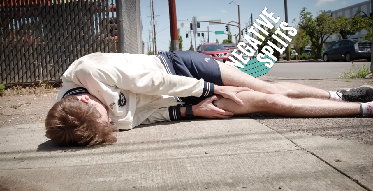 A white man in running gear clutching his right quad while laying on the sidewalk.