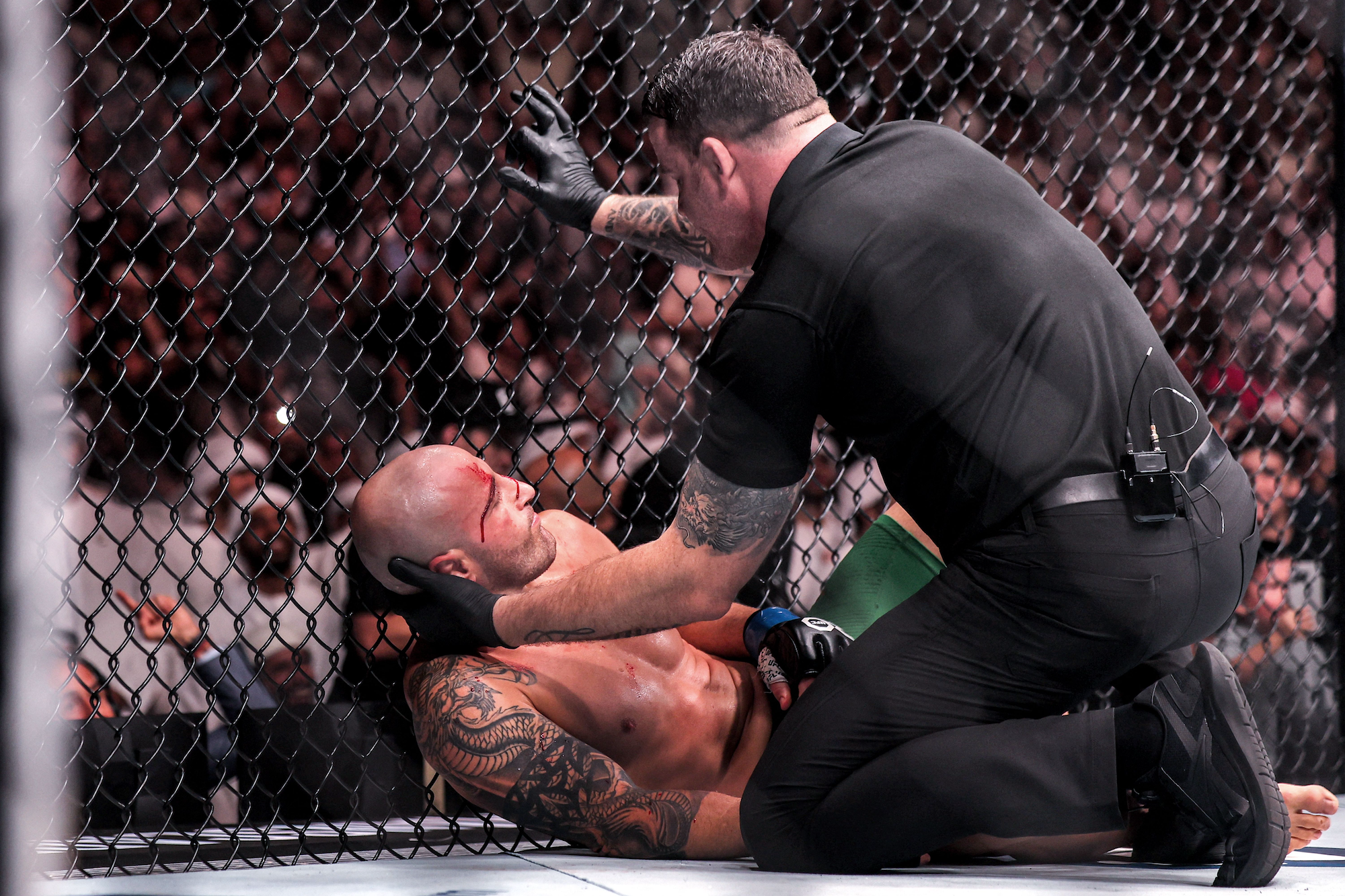 A UFC referee cradles the head of Alexander Volkanovski, crumpled against the fencing at the end of his match against Islam Makhachev