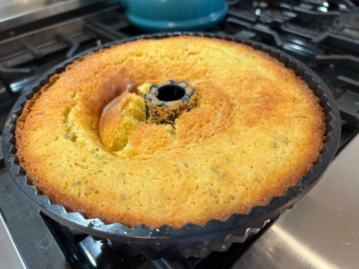 A baked bundt cake, still in the tin, with alarming signs of a cave-in on the left side.