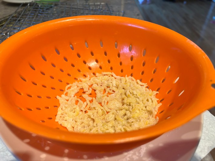 Small strips of candied lemon peel sit in an orange plastic colander.