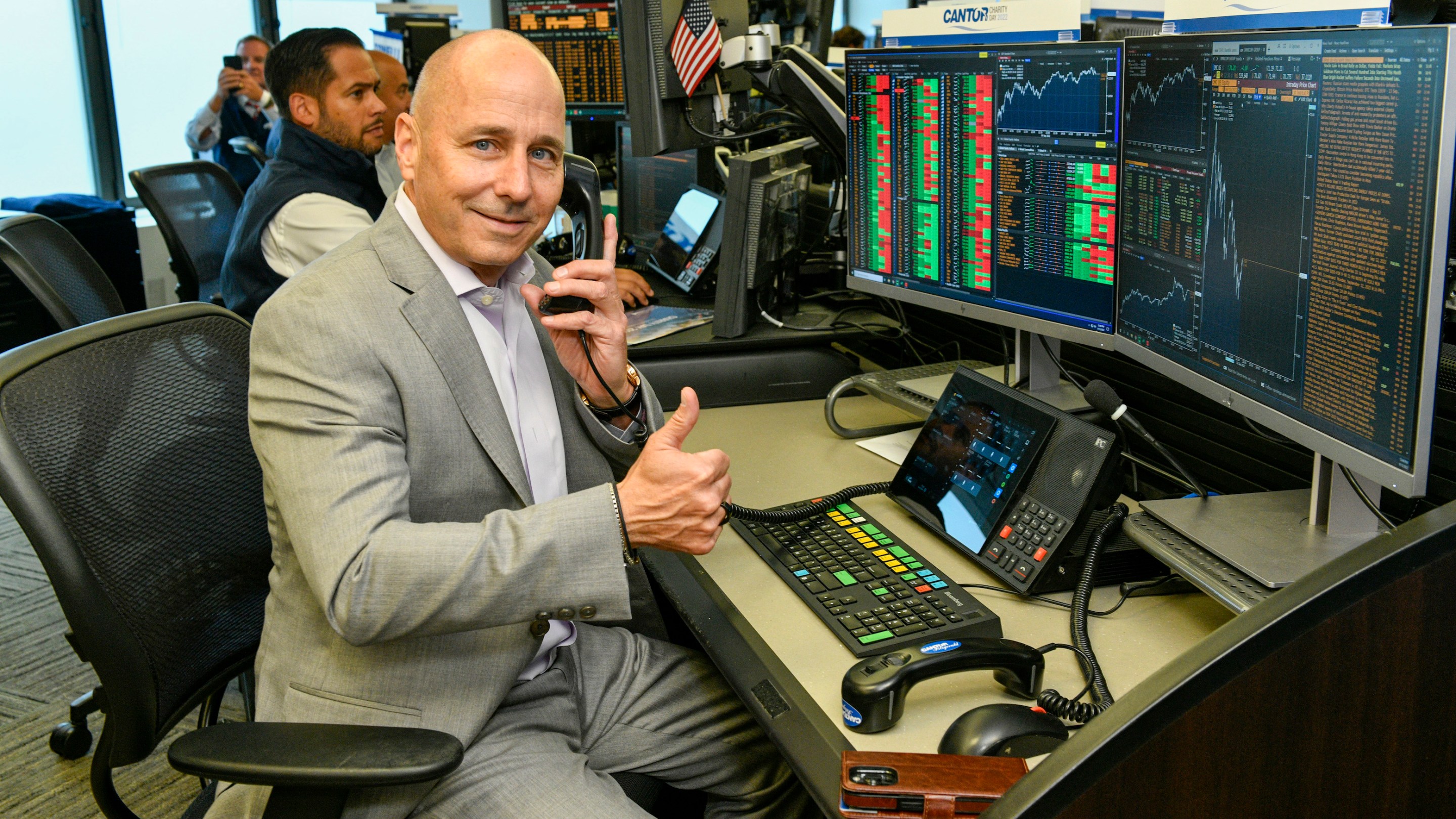 Brian Cashman sitting at a Bloomberg training terminal and giving a goofy thumbs up at a charity event in 2022.