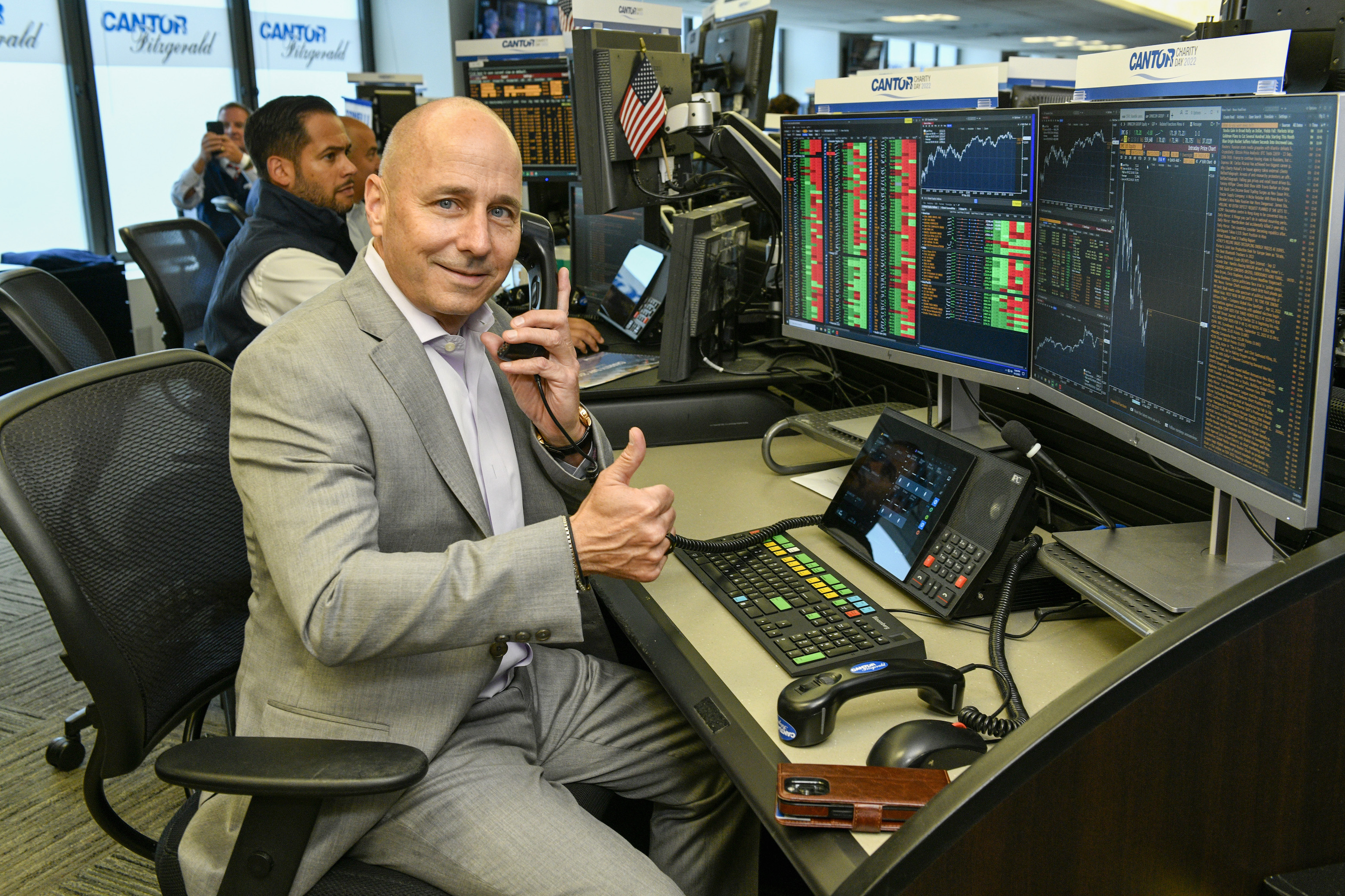 Brian Cashman sitting at a Bloomberg training terminal and giving a goofy thumbs up at a charity event in 2022.