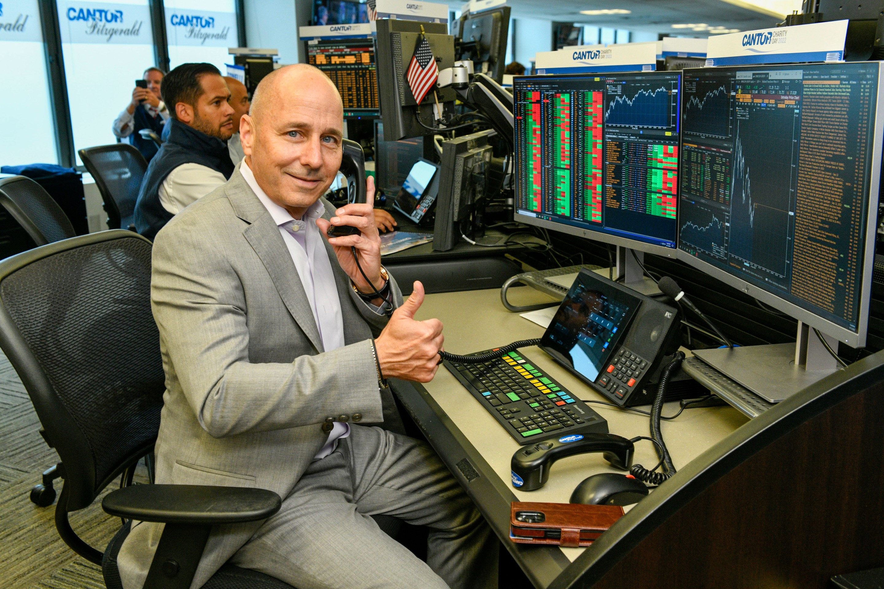 Brian Cashman sitting at a Bloomberg training terminal and giving a goofy thumbs up at a charity event in 2022.