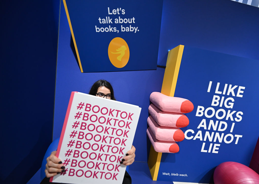 A woman stands behind an oversized book with "#BookTok" on the cover in a colorful exhibit on BookTok at the Frankfurt Book Fair, October 2023