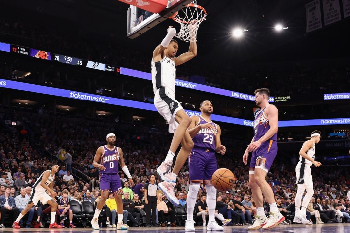 Eric Gordon of the Suns looks expectantly towards his bench as Victor Wembanyama dunks directly over him.