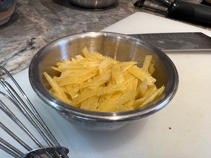 A small metal bowl holds a pile of tiny sliced lemon peels.