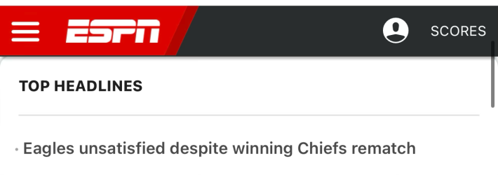 Screenshot from ESPN. At the top there is a bar that is about 75% black (right side) and 25% red (left side). The red side has ESPN logo, then there's a slash type thing (Defector's influence, I'm sure) and then on the right side, the black side, it says scores and a little username image.Then it says TOP HEADLINES• Eagles unsatisfied despite winning Chiefs rematch