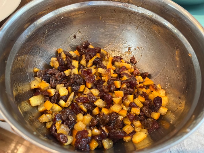 Raisins, cranberries, and candied orange peel are mixed with brown sugar in a large metal bowl.