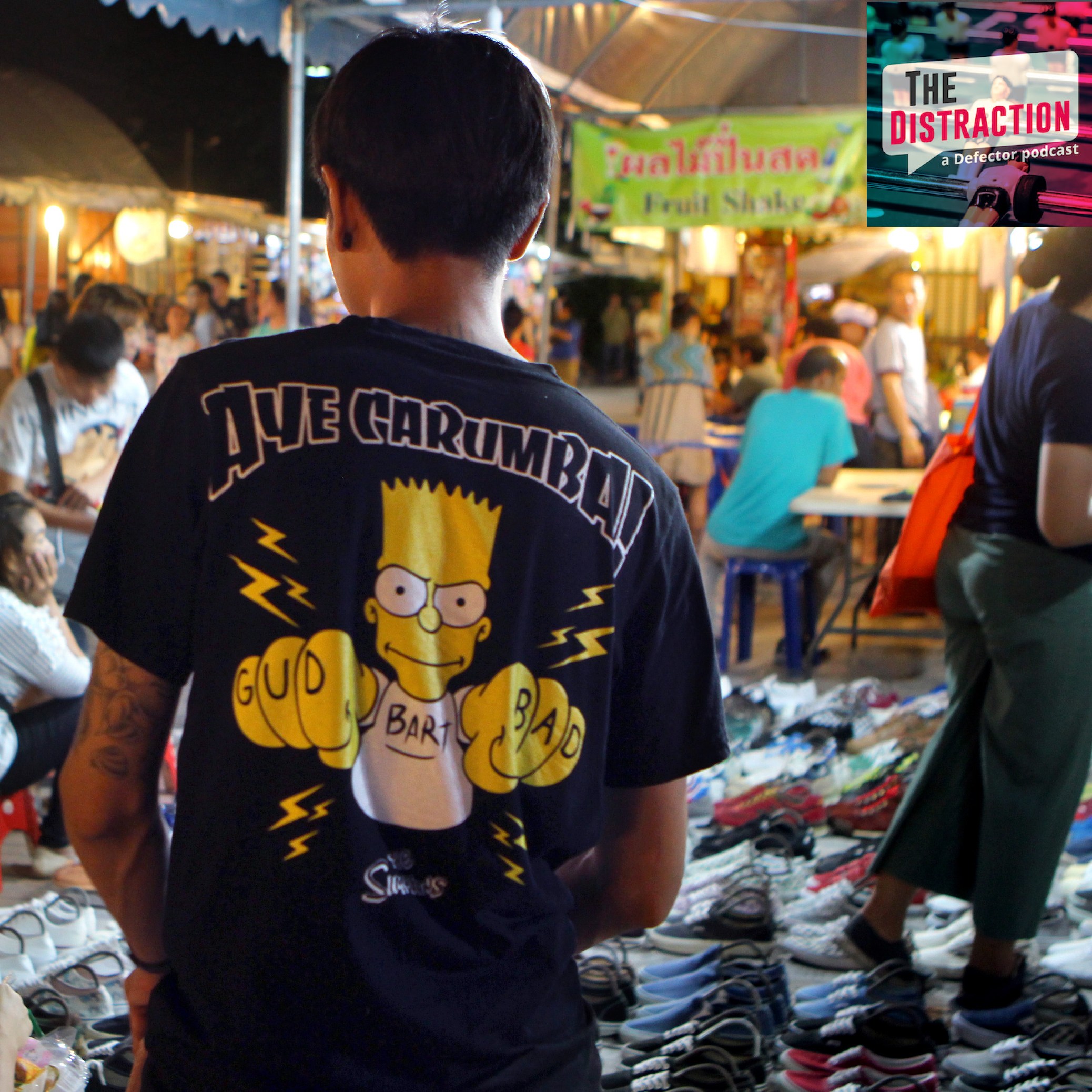 A man wears a bootleg Bart Simpson t-shirt—black, with the words Ay Carumba (sic) in heavy metal font over an image of Bart displaying GUD and BAD finger tattoos—on the streets of Bangkok, in 2018.