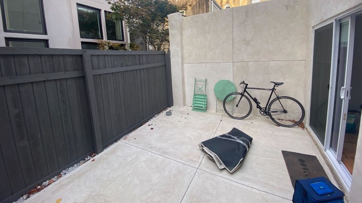 Luis's new backyard lot, with a table, bike, folded up rug, mat, and cooler. It's a mess.