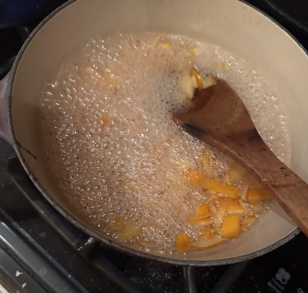Orange peels in a saucepan with wooden spoon.